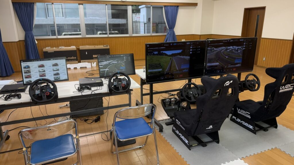 4台並んだレーシングゲーム機材と活動会場の様子